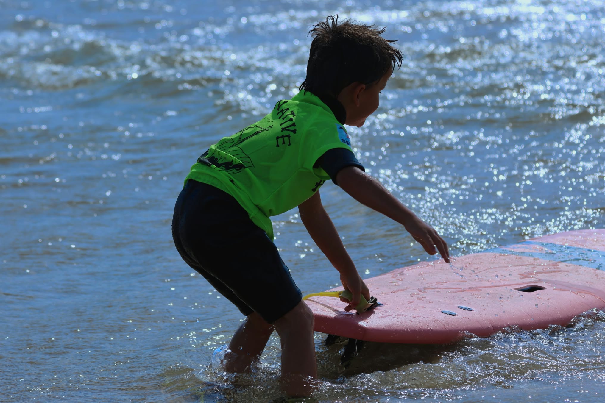 Jeune surfeur en vert préparant sa planche rose dans l'eau