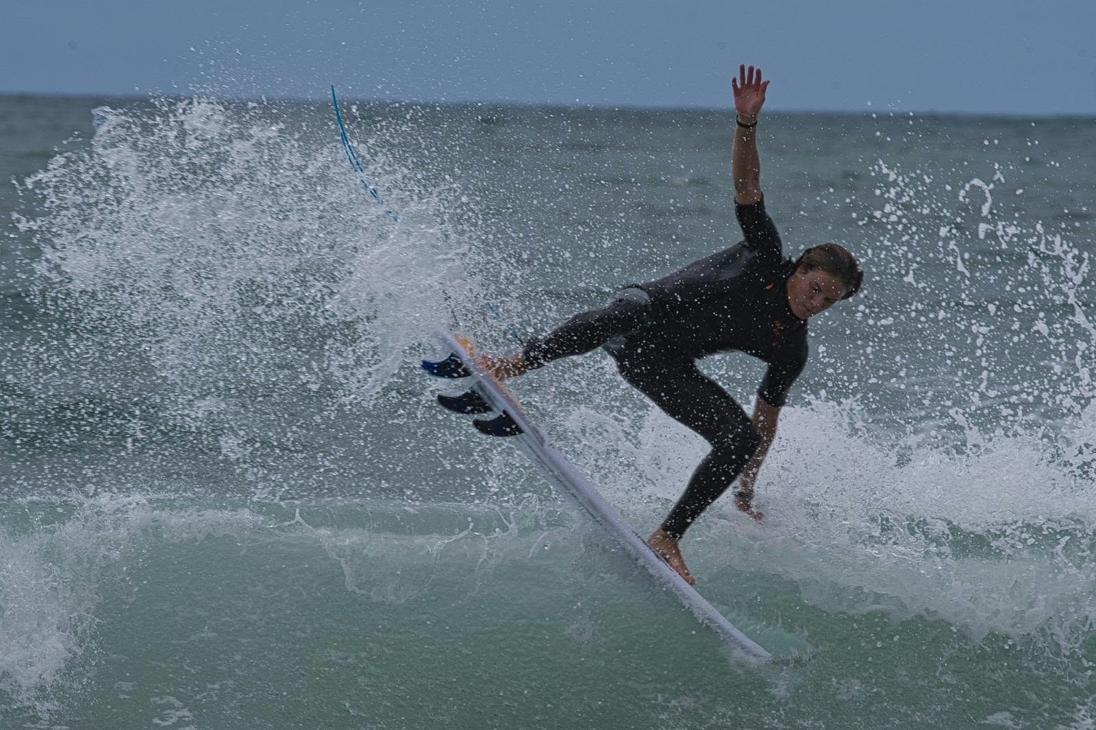 Surfeur en combinaison noire dans une gerbe d’écume